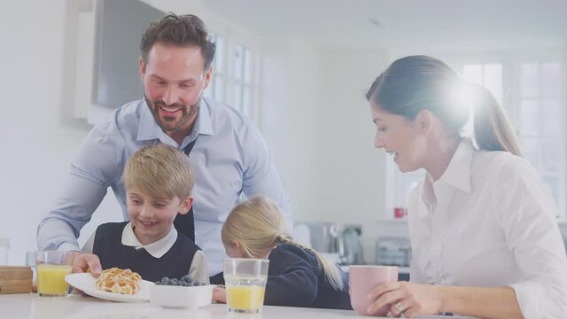Medium shot of two children wearing school uniform in kitchen eating breakfast waffles as parents get ready for work - shot in slow motion