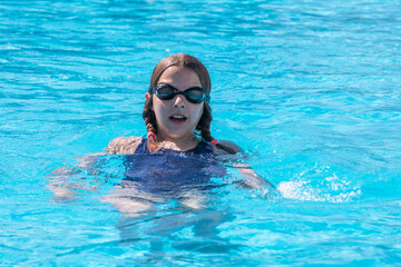 happy girl swims on her back in the pool wearing swimming goggles, horizontal.