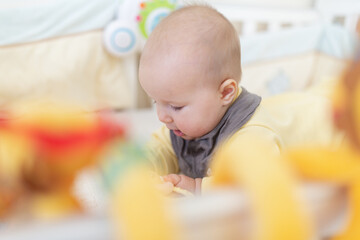 Caucasian blonde baby five months old lying on bed at home. Kid wearing cute clothing trendy colors: ultimate gray and illuminating. Infant playing with toys