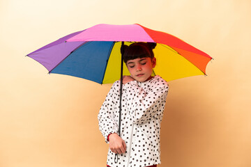 Little girl holding an umbrella isolated on beige background suffering from pain in shoulder for having made an effort