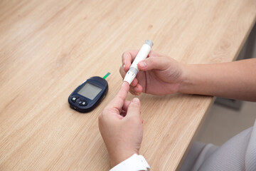 Close up of woman hands using lancet on finger to check blood sugar level by Glucose meter using as...