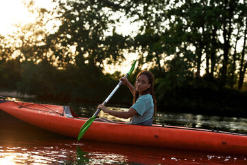 Relaxed young woman looking aside while paddling kayak on a lake surrounded by nature