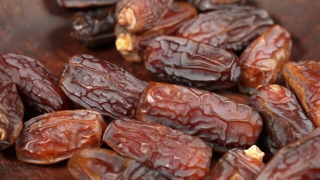 Closeup 4K video footage of tasty brown dried dates fruit isolated on brown background. Woman grabbing fruits from brown plate