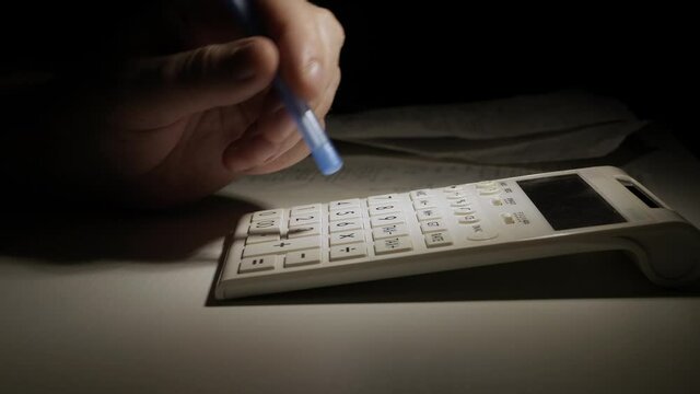 Businessman Working Late, with Invoices, Makes Financial Calculations with Adding Machine. Accounting Fee and Taxes Calculations.