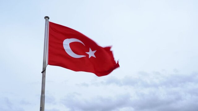 Closeup view 4k stock video footage of red flag of Turkey blowing by strong wind outdoors. Flag isolated on cloudy sky background