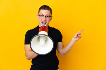Young caucasian man isolated on yellow background shouting through a megaphone and pointing side