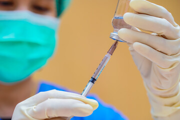Medical team  in full uniform holding syringe taking covid 19 corona virus vaccine from vial bottle...