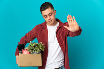 Young caucasian man making a move while picking up a box full of things isolated on blue background...