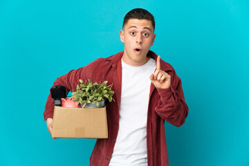 Young caucasian man making a move while picking up a box full of things isolated on blue background...