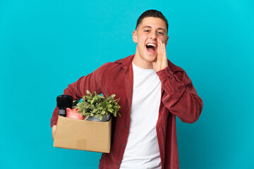 Young caucasian man making a move while picking up a box full of things isolated on blue background shouting with mouth wide open