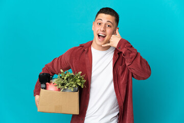 Young caucasian man making a move while picking up a box full of things isolated on blue background...