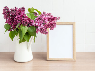 Bouquet of lilac flowers in a vase and empty wooden frame