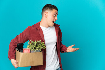 Young caucasian man making a move while picking up a box full of things isolated on blue background...
