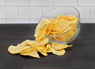A glass bowl of potato chips spilling onto a tabletop.