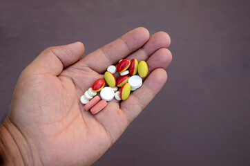 closeup bunch the pink ,white with red,yellow color small medicines tablet, capsule hold hand health care medical concept isolated on purple background.