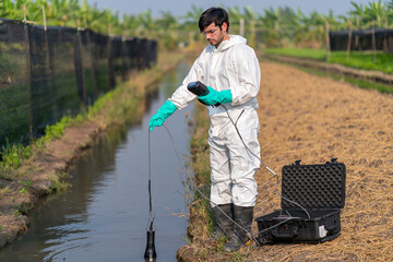 Man technician in full body protective suit collecting sample of water .Portable water quality measurement .Water quality for agriculture. Checking water ph on field.