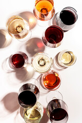 Red, rose and white wine in glasses on white background, top view. Wine bar, shop, winery, wine tasting concept. Hard light and harsh shadows