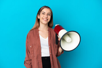Young caucasian woman isolated on blue background holding a megaphone and smiling a lot