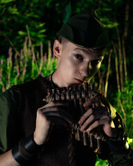 Peter Pan plays a flat sitting in the grass against the backdrop of the forest. Cosplay on Peter Foam. Robin Hood