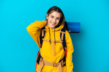 Young mountaineer woman with a big backpack isolated on blue background laughing