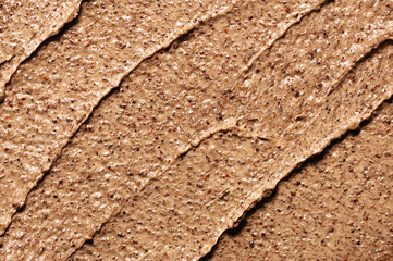 Smears of organic brown scrub with small dark grains for face and body gentle peeling as background macro view from above.