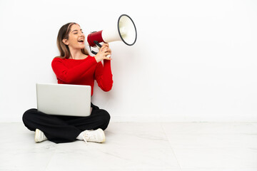 Young caucasian woman with a laptop sitting on the floor shouting through a megaphone