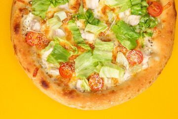Pizza with tomatoes and salad on a yellow background.