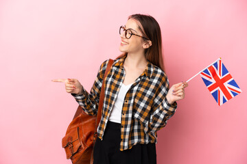 Young hispanic woman holding an United Kingdom flag isolated on pink background pointing finger to the side and presenting a product