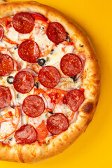 Pizza with pepperoni and tomato. On a yellow background.