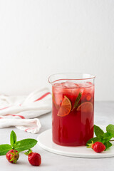 Fresh strawberry and lime drink with ice and rosemary in a jug close-up, summer refreshing lemonade