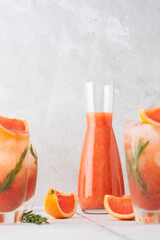 Cold refreshing grapefruit smoothie with rosemary and ice in glasses, grapefruit wedges and rosemary sprigs on the table, home party