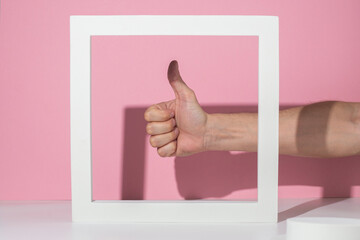 Male hand showing thumb up in white square podium for presentation on pink background