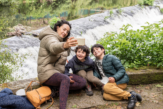 mother with her son and her daughter taking a picture with the phone while sitting by the river