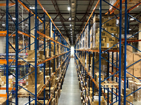Perspective view to the warehouse, blue metal racks, shelves full of goods packed in carton boxes or pallets. Clean and tydy distribution center. 
