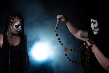 Two supernatural entities at war, one using a rosary against the other, black background, Low Key portrait, selective focus.