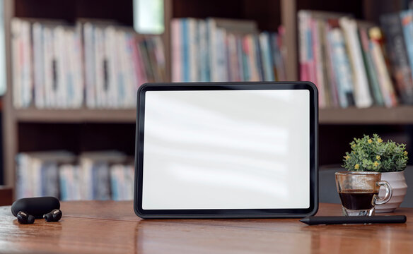 Mockup blank screen tablet on wooden table with blurred bookshelf background.