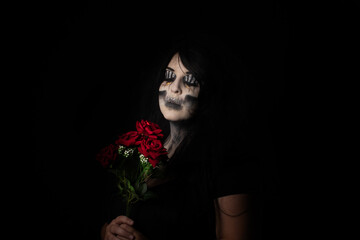 Bride cadaver with black veil holding a bouquet of red roses, black background, Low Key portrait, selective focus.