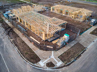 An aerial view of three houses on a corner during the frame stage of construction, almost like a...