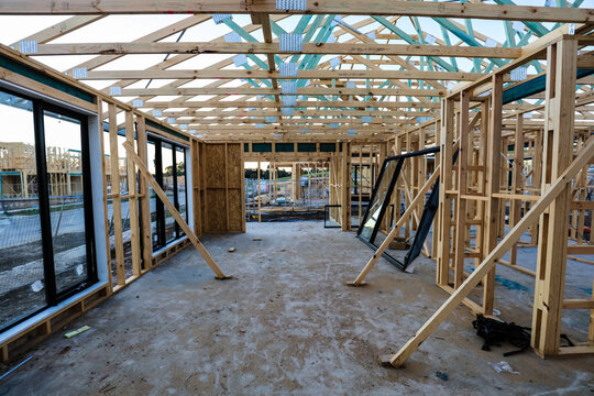 The inside of a house during the early stages of construction, some windows installed, braces holding the frame in place, and another house in the next lot that is also beginning to be built.