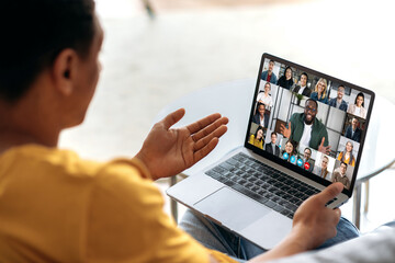 Distant communication using app and laptop. The guy sits on the couch, uses a laptop to communicate with colleagues or friends via video conference, virtual meeting, telecommunication concept