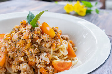 Spaghetti stir-fried with tomato sauce and minced chicken in hot Thai style. Tender and delicious served in a white plate placed on a wooden table, resulting in a delicious spaghetti from the sauce.