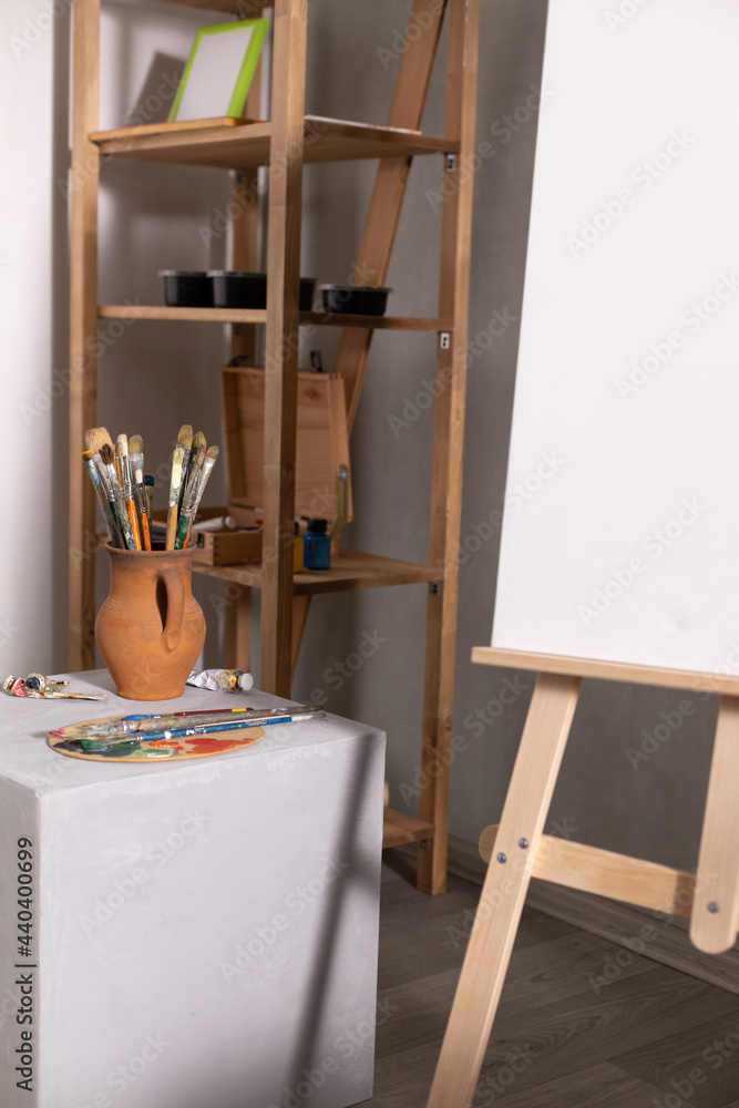 Poster Paint brush in clay jug and palette at cube. Art still life and canvas with painter tool