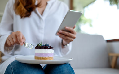 Closeup image of a young woman using mobile phone while eating cake in cafe