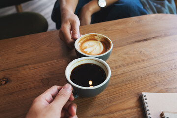 Fototapeta na wymiar Closeup image of a man and a woman clinking white coffee mugs in cafe