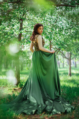A beautiful girl in a long green dress in blooming apple trees.