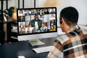 Online video communication. Over shoulder view of mixed race man, on computer screen with...