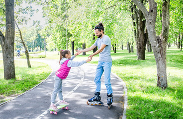 Obraz premium Family activities in the summer park. Happy father teaching little daughter to roller skating in park. A good father spends time with his child.