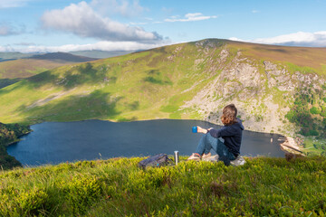 Woman having a cup of coffee and enjoying the view over Lough Tay after a hiking in Wicklow...
