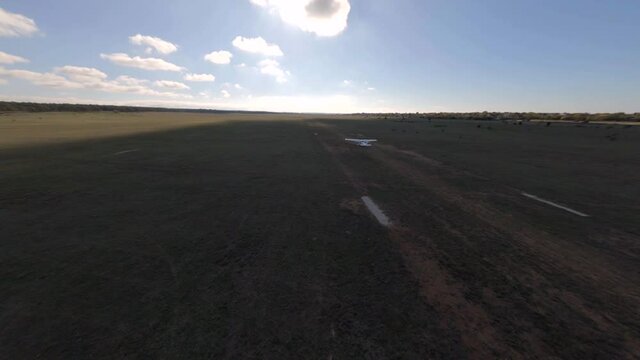 Fpv drone follows sports aeroplane taking off from ground runway with signal marks among endless fields under blue sky with small clouds