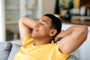 Relaxed satisfied calm hispanic guy in a yellow t-shirt, resting on the sofa at home with his eyes...